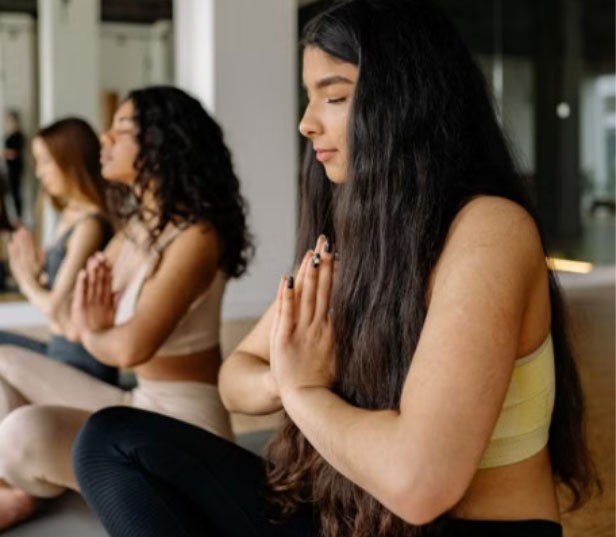 Three women seated in a row with their eyes closed and their hands pressed together at their chests