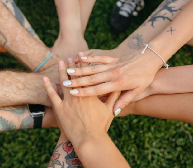 A circle of hands stacked on top of one another on the grass