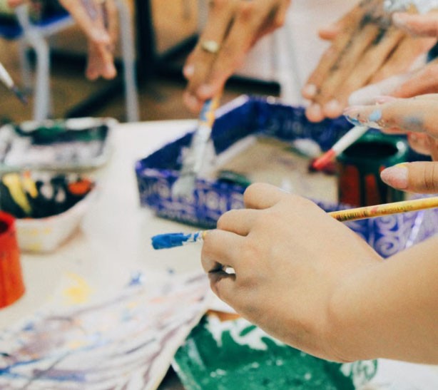 Hands painting with brushes around a table of paint pots at a creative workshop