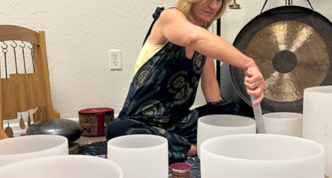 Dr. Tanya Lea seated among crystal singing bowls in the studio, with a gong and a chime behind her
